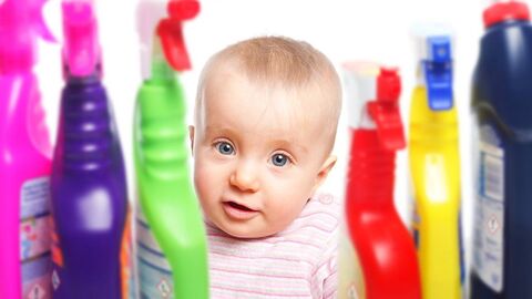 Chemikalien von Kindern fernhalten Ein Baby schaut zwischen bunten Putzmittelflaschen in die Kamera