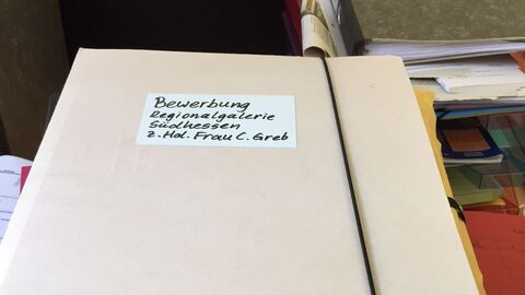 Bewerbung  Ein Papierstapel, auf dem oben eine Bewerbungsmappe für die Regionalgalerie Südhessen liegt.
