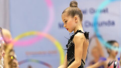 Jugendarbeit Ein junges Mädchen mit einem schwarzen, mit Pailletten und Glitzer besetzen Turntrikot bei einem Turnwettbewerb