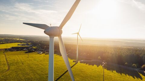 Aufnahme einer Windkraftanlage aus der Luft, im Hintergrund sieht man Felder im Sonnenschein