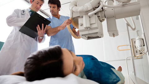 Röntgen Ein Arzt hält das Röntgengerät über eine Patientin und berät sich mit einem Kollegen
