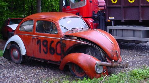 Autowrack Ein altes rotes Auto, mit Graffiti besprüht und abgefallener Radkappe, steht auf einem Parkplatz im Wald