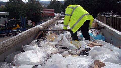 Ein Mann mit gelber Warnjacke steht auf einem Abfalltransporter