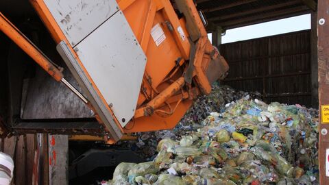 Ein oranger Container kippt Müllsäcke auf einen Haufen