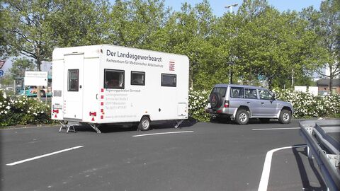 Aktion Arbeitsschutz-Mobil Ein weißer Anhänger mit der Aufschrift "Landesgewerbearzt" steht am Straßenrand