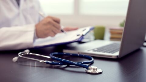 Die Arbeitsmedizin befasst sich mit Wechselbeziehungen zwischen Arbeit und Mensch Arzt sitzt an seinem Schreibtisch und notiert etwas auf dem Klemmbrett