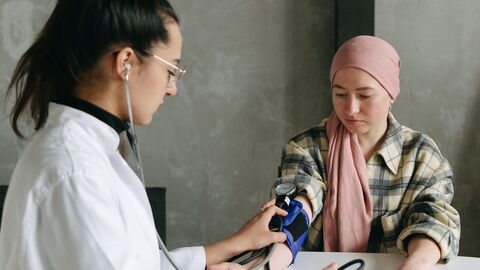 Für unter 18 Jährige ist eine Untersuchung vor der Ausbildung Pflicht Eine Ärztin im weißen Arztkittel misst einer jungen Frau den Blutdruck