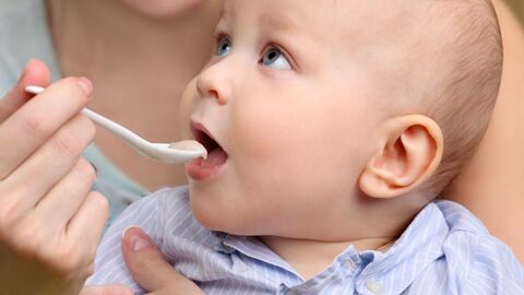 Baby auf dem Schoß einer Frau, welches mit Brei gefüttert wird