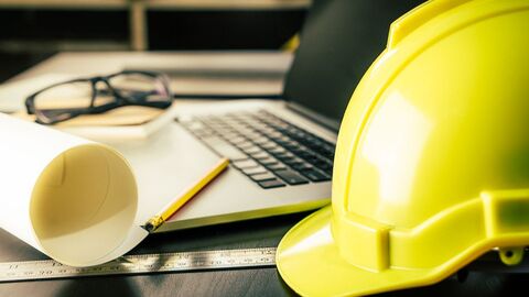 Bauhelm, Bauzeichnungen liegen neben Laptop auf dem Schreibtisch