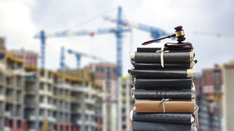 Baurecht (Symbolbild) Bücherstapel, darauf liegt ein Gerichtshammer, im Hintergrund Rohbauten