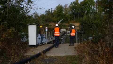 Gewässerbenutzung im Tagebaubetrieb Drei Männer mit Warnweste von hinten am See