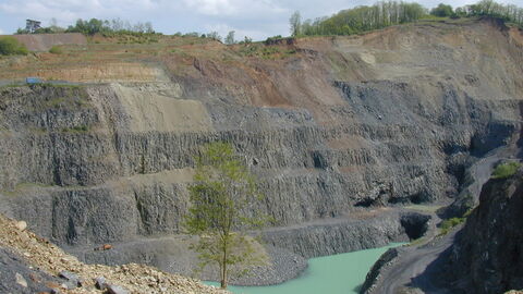Basalt-Tagebau Zu sehen sind die graue Steinwände eines Tagebaus und türkises Wasser.