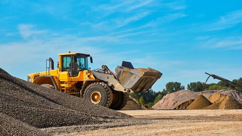 Ein gelber Bagger zwischen mehreren Kiesbergen 