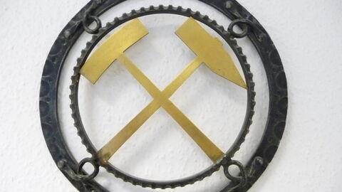 Schlägel und Eisen Ein rundes Metallwappen mit dem goldenen Symbol Schlägel und Eisen.