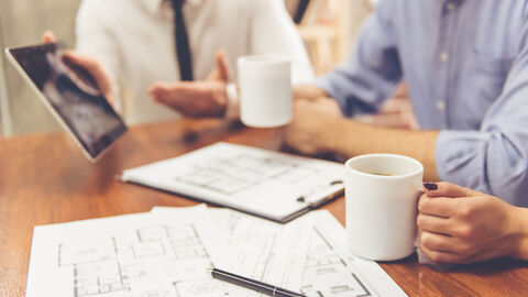 Drei Personen sitzen am Tisch, auf dem Grundrisspläne eines Gebäudes liegen