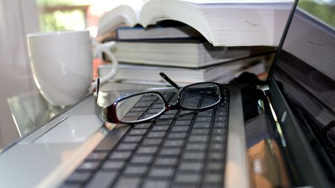 Schreibtisch Computer, Bücher und Tasse auf einem Schreibtisch, auf der Tastatur liegt eine Brille