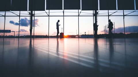 Menschen stehen mit Gepäck in einer Flughafenhalle und warten
