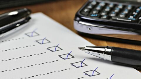 Eine Checkliste und ein Kugelschreiber liegen auf einem Tisch, im Hintergrund sieht man einen Taschenrechne