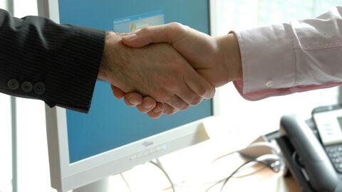 Händedruck Zwei Männer reichen sich die Hand. Im Hintergrund ist ein Computerbildschirm.