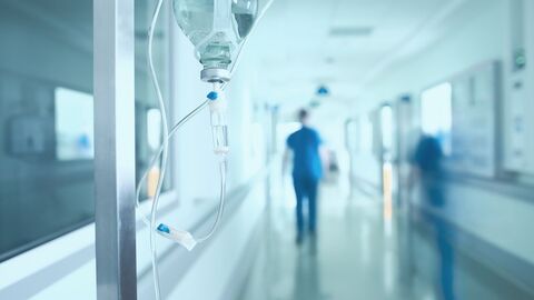 Im Krankenhaus Langer Krankenhausflur, Infusionsflasche im Vordergrund, zwei Personen eilen über den Gang
