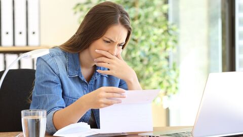 Junge Frau sitzt an ihrem Büroarbeitsplatz und blickt betroffen auf ein Schriftstück