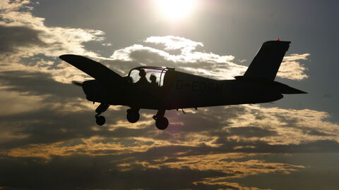 Die Silhouette eines Kleinflugzeuges am Himmel während der Dämmerung