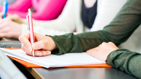 Hand einer Seminarteilnehmerin, die sich Notizen macht Eine Seminarteilnehmerin macht sich mit einem Stift Notizen
