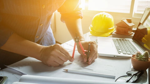 pruefingenieur Architekt arbeitet an seinem Arbeitsplatz mit Zirkel, Laptop und Stift