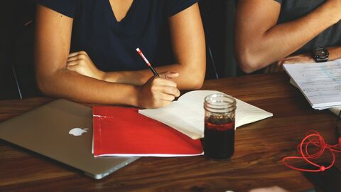 Seminarteilnehmerin Zwei Personen sitzen mit Schreibunterlagen, Laptop und Getränk am Tisch.