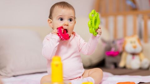spielendes Kleinkind Baby sitzt auf einer Decke und steckt sich einen Beißring in den Mund