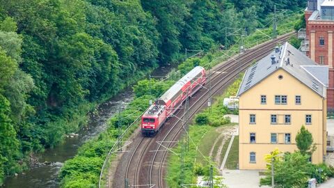 Ein Zug fährt auf einer Bahnstrecke zwischen Wald und Gebäuden entlang