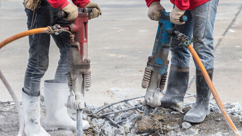 Zwei Männer bohren mit zwei Presslufthammern in den Beton