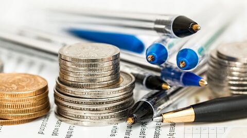 Papiere, Geldmünzen und Kugelschreiber liegen durcheinander auf einem Tisch