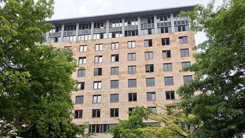 Mehrstöckiges Bürogebäude, davor stehen mehrere Laubbäume