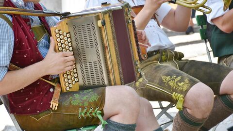 Musiker im Biergarten Ein Trompeter und ein Akkordeonspieler im Trachtenanzug spielen im Biergarten