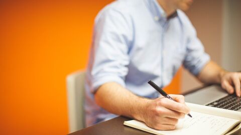 Ein Mann sitzt an einem Schreibtisch und schreibt etwas in ein Heft