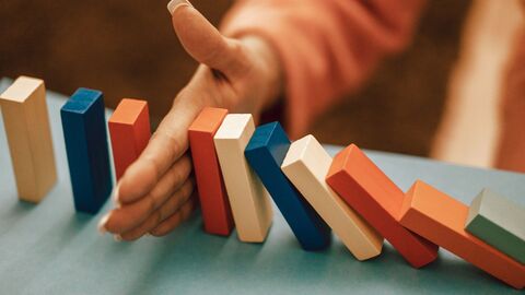 Eine Hand greift in eine Dominoreihe ein und stoppt so die Kettenreaktion