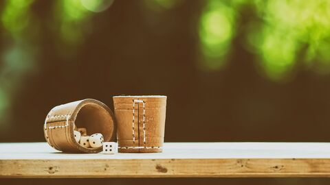 Zwei Würfelbecher auf einem Holzbrett, im Hintergrund verschwommenes Grün
