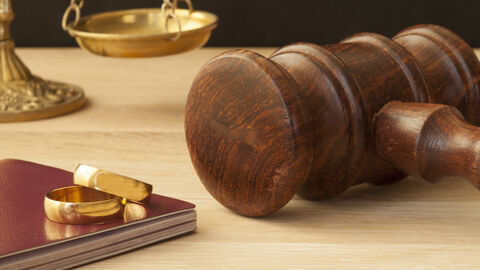 Scheidung Eheringe und Hammer liegen auf einem Tisch, im Hintergrund eine Waage