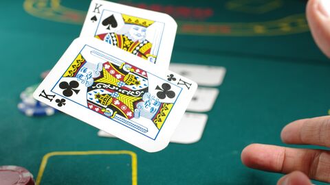 Poker Eine Hand wirft zwei Spielkarten auf den Pokertisch, im Hintergrund liegen Pokerchips