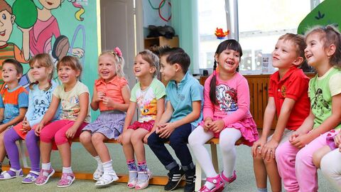 Kinder Viele Kinder sitzen im Kindergarten auf einer Bank und lachen