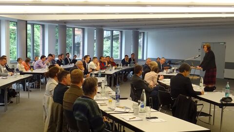 Regierungspräsidentin Brigitte Lindscheid spricht zu den Teilnehmenden in Frankfurt.  Saal mit Menschen an Tischen - vorne spricht jemand