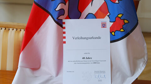 Verleihungsurkunde zur Anerkennungsprämie Eine Urkunde vor einer Hessischen Fahne