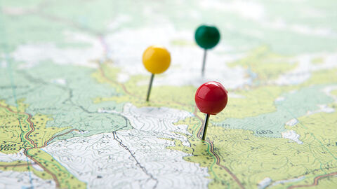 Geografie (Symbolbild) Landkarte, auf der mit drei bunten Stecknadeln bestimmte Stellen markiert sind