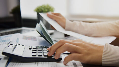 Person am Schreibtisch mit Papieren und Taschenrechner