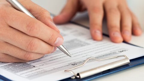 Formular auf einem Klemmbrett, das gerade mit Kugelschreiber ausgefüllt wird