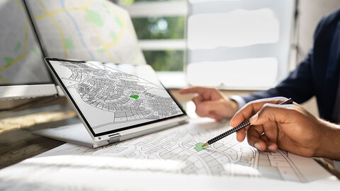 Zwei Geschäftsleute sitzen vor Karten und deuten auf einzelne Grundstücke