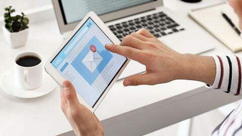 Person am Schreibtisch mit Tablet-PC in der Hand, eine neue E-Mail ist eingegangen