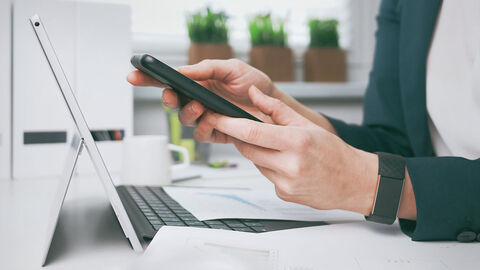 Eine Person am Schreibtisch mit Tablet-PC, Handy und Papieren