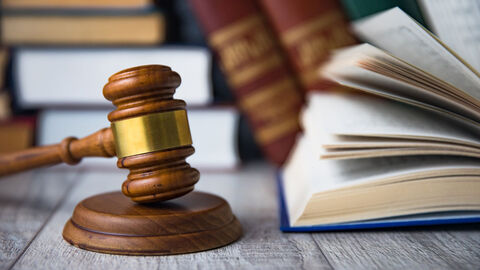 Auf einem Holztisch liegen mehrere Bücher und ein Gerichtshammer